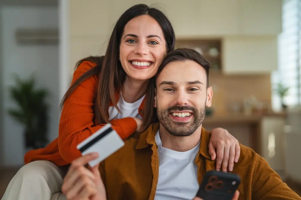Smiling couple at home holding a credit card and phone