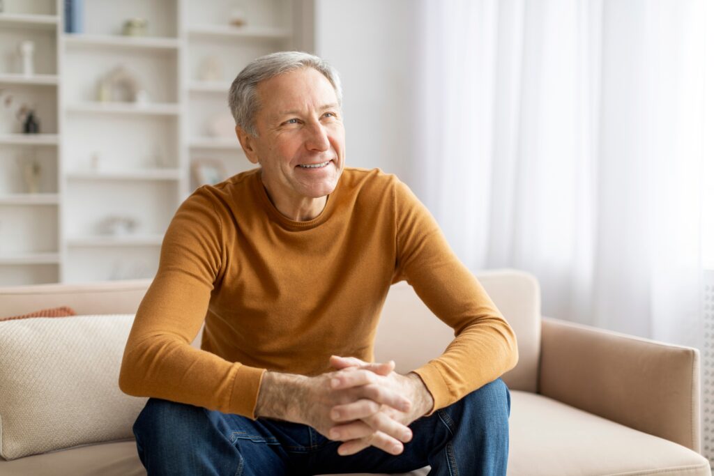 Smiling older man seated on a sofa, hands clasped